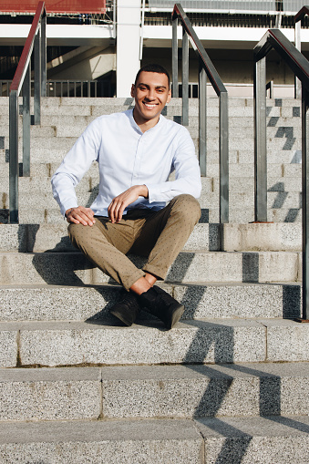 Young smiling mixed race man sitting on the staircase outside
