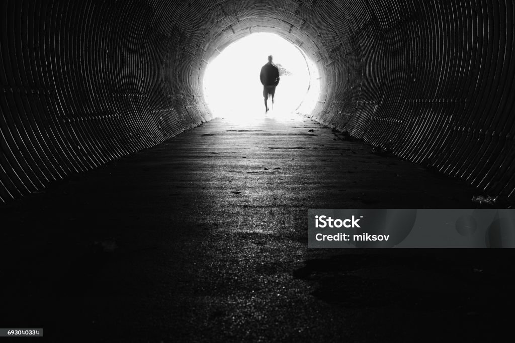 Light at the end of the tunnel with silhouette of man Dark tunnel with light end. Silhouette man on the end. Tunnel Stock Photo