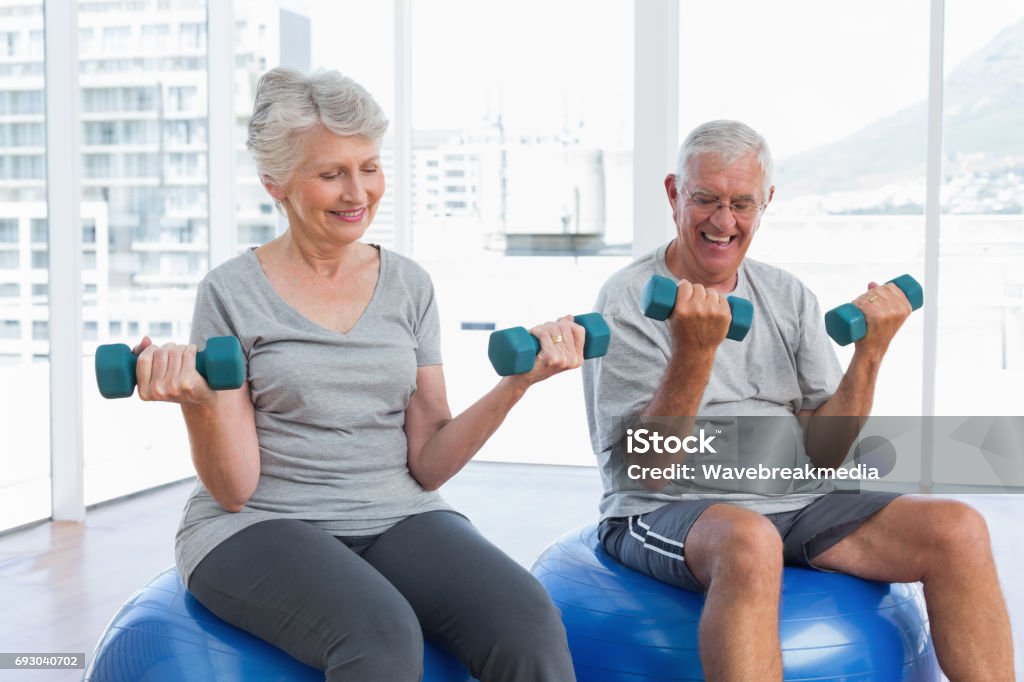 Felice coppia senior seduta su palle fitness con manubri - Foto stock royalty-free di Terza età
