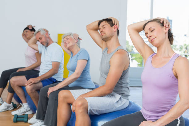 istock Class sitting on exercise balls and stretching neck in gym 693070340
