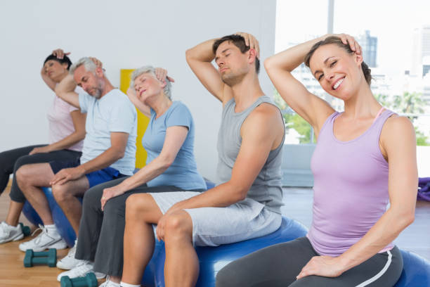 istock Class sitting on exercise balls and stretching neck in gym 693070374