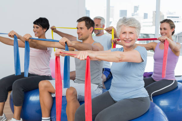 istock Class holding out exercise belts while sitting on fitness balls 693087886