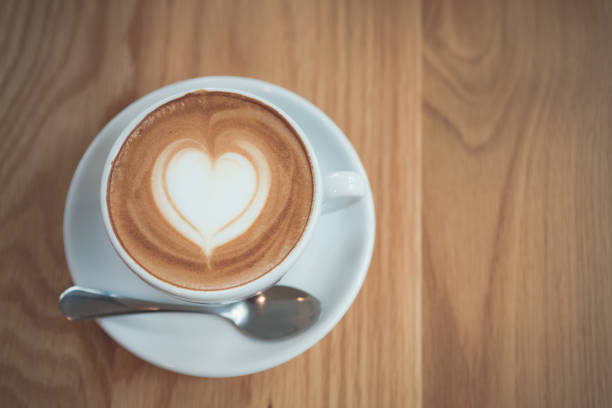 Cappuccino or Latte coffee art cup with heart shaped surface, top view, on wooden table.