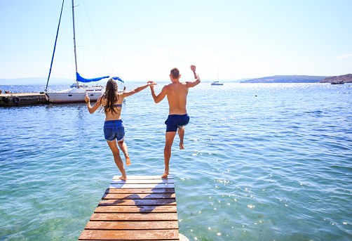 Rear view of couple holding hands and jumping into water from a pier.