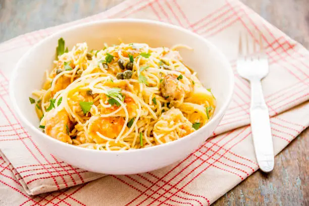 Chicken piccata angel hair in a bowl close-up horizontal image.