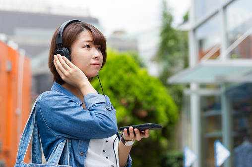 Japanese young woman listening to music on the street with headphones.
