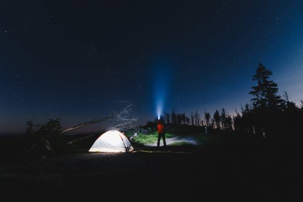 istock Tourist with flashlight near his camp tent at night 693148588