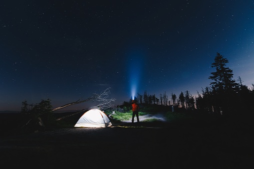 Man tourist with flashlight near his camp tent at night. Malinowska Skala. Szczyrk. Silesian Beskid, Poland