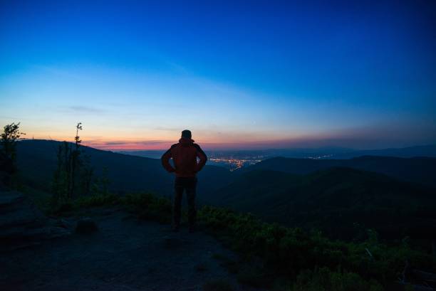 istock Man tourist standing on mountaintop observing city lights. 693148816