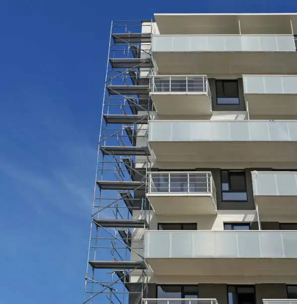 Fragment of a new inhabited apartment house and metal building constructions against the background of the blue summer sky