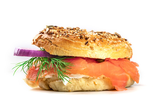 A side view of a bagel with cream cheese, lox, purple onions, capers, and dill, on a white background with a place for text