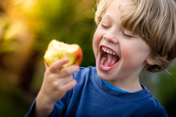 cute blonde child about to take a bite of an apple - child eating imagens e fotografias de stock