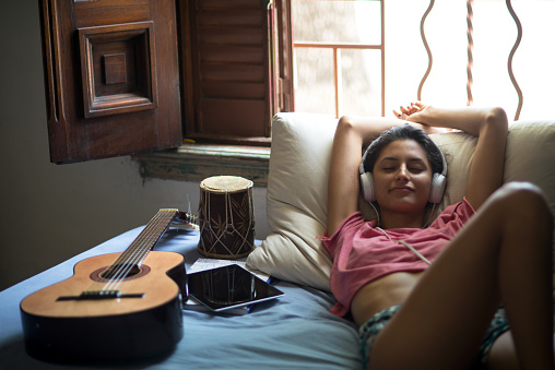 Woman laying down at the bad and listening to music at home with smile at her face