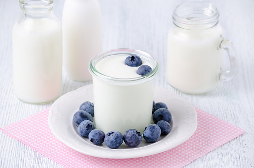 a cup of yogurt with blueberrys and different bottles of drink yogurt and milk on a plate, napkin on the table