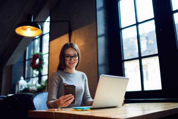 Busy attractive business woman in glasses checking email box via smartphone Waiting for feedback from colleague while working in cafe interior making distance job project using laptop and wifi Automotive Smartphone Integration stock pictures, royalty-free photos & images