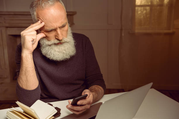 istock pensive grey haired man sitting at table and using smartphone at home 693224272