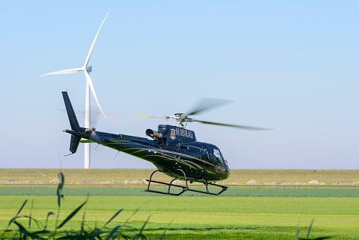 American Eurocopter AS350 helicopter taking off from a field in The Noordoostpolder, The Netherlands during a beautiful summer day. The helicopter is photographed from the public accessible road next to the field near the town of Urk in Flevoland, The Netherlands.