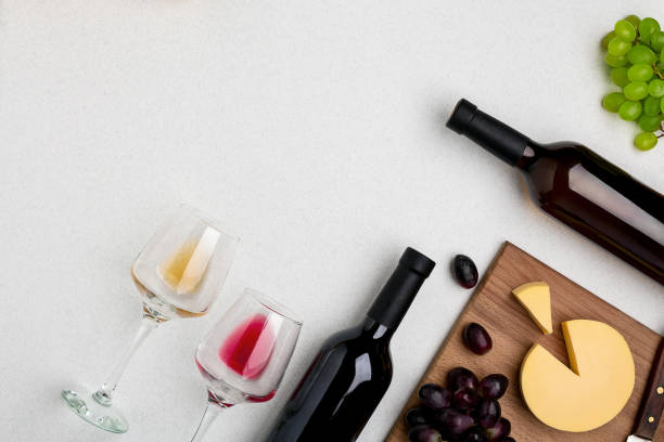 due bicchieri da vino con vino rosso e bianco, bottiglie di vino rosso e vino bianco, formaggio su sfondo bianco. vista orizzontale dall'alto - paio foto e immagini stock