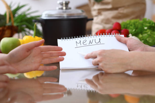 istock Human hands pointing into note book with copy space area. Two woman making menu in the kitchen, closeup. Cooking and friendship concept. 693254776