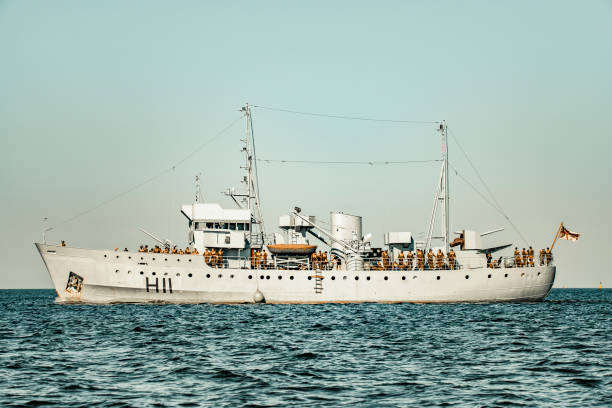 Old naval war ship sailing on open water towards the set of Christopher Nolan's Dunkirk on the IJsselmeer near Urk in The Netherlands. Actors dressed up as soldiers are standing on the deck of the former Navy Pilot Vessel that has been converted to a WWII ship. The ship is photographed from the public accessible shore of the IJsselmeer in the town of Urk in Flevoland, The Netherlands.