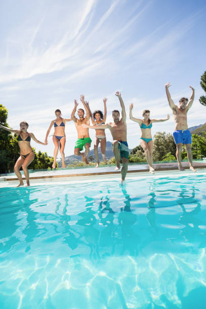 Group of friends jumping in swimming pool Group of friends jumping in swimming pool with their hands raised half dressed girls pictures stock pictures, royalty-free photos & images