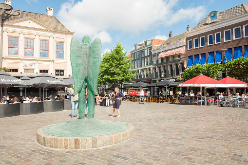 Grand Place or Grote Markt in Zwolle, The Netherlands during springtime. People are looking at the glass Angel statue and sitting at the cafes around the market square.