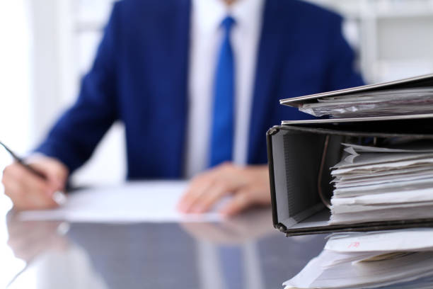 istock Binders with papers are waiting to be processed with businessman back in blur. Accounting planning budget, audit, insurance  and business concept 693263384
