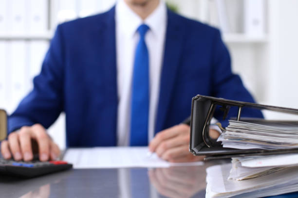 istock Binders with papers are waiting to be processed with businessman back in blur. Accounting planning budget, audit, insurance  and business concept 693264220