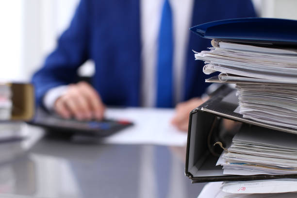 istock Binders with papers are waiting to be processed with businessman back in blur. Accounting planning budget, audit, insurance  and business concept 693264512