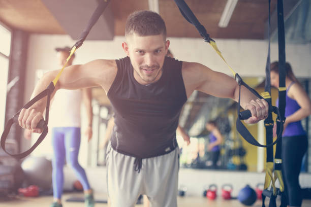 istock Young man workout in healthy club. Man doing exercise with strip  system. 693272496