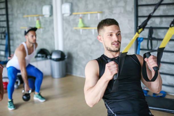 istock Young man workout in healthy club. Man doing exercise with strip  system. 693272506