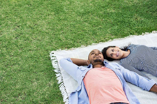 Young multiethnic couple lying on blanket on grass. Latin woman with her african boyfriend relaxing on picnic blanket outdoor. Mature happy couple in love lying on grass with copy space.