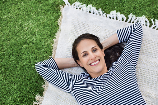 A smiling Caucasian woman lying in bed in her black nightgown, holding a pillow and daydreaming.