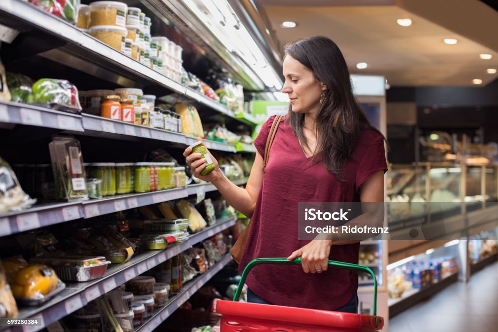 Woman shopping in supermarket Young woman shopping in grocery store. Mature woman checking food label in supermarket. Latin woman holding shopping basket and choose a product in supermarket. Supermarket Stock Photo