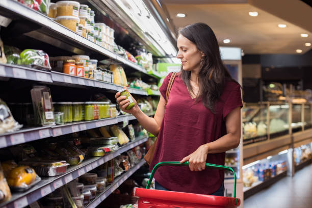 Woman shopping in supermarket Young woman shopping in grocery store. Mature woman checking food label in supermarket. Latin woman holding shopping basket and choose a product in supermarket. nutrition label stock pictures, royalty-free photos & images