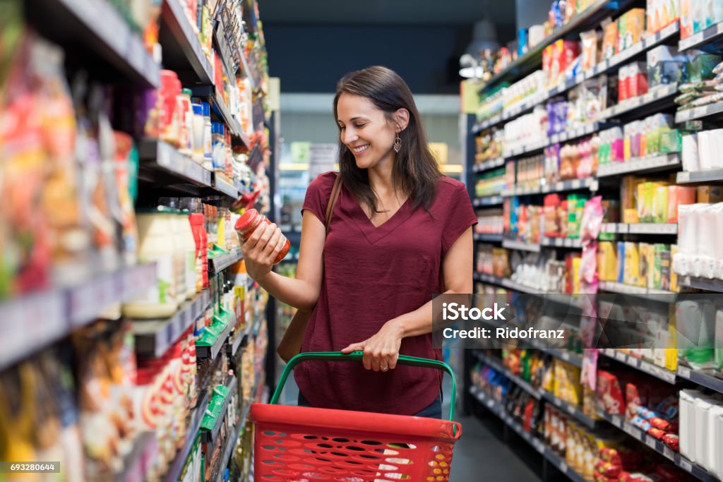 Smiling woman at supermarket Happy mature woman looking at product at grocery store. Smiling hispanic woman shopping in supermarket and reading product information. Costumer buying food at the market. Supermarket Stock Photo