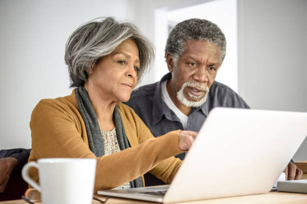 pareja senior afroamericano en portátil junto con expresión seria - home finances couple computer african ethnicity fotografías e imágenes de stock