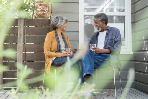Senior African American couple sitting in garden with drinks They are sitting on chairs on the decking talking and relaxing over drinks 60 69 years stock pictures, royalty-free photos & images