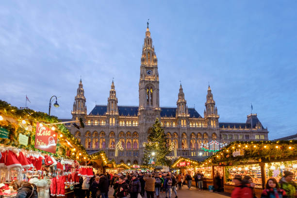 Vienna at Christmas, Rathausplatz & Vienna City Hall - Austria Tourists and locals at the Christkindlmarkt in the Rathausplatz, the most important Christmas Market of the city. In the background stands the imposing Vienna City Hall, a beautiful example of Gothic Revival architecture dating back to the late nineteenth century. vienna city hall stock pictures, royalty-free photos & images