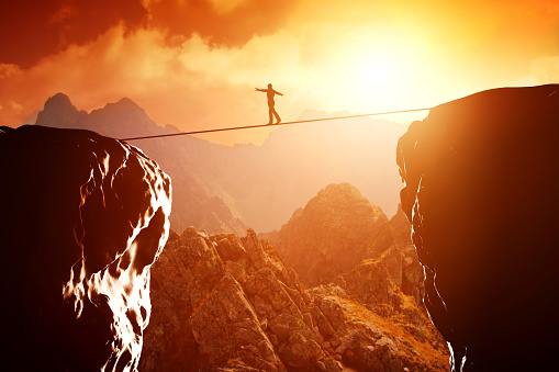 Man walking and balancing on rope over precipice in mountains at sunset