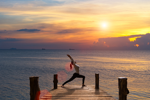 Meditation girl on the sea during sunset on the wood the bridge. Yoga silhouette. Fitness and healthy lifestyle.