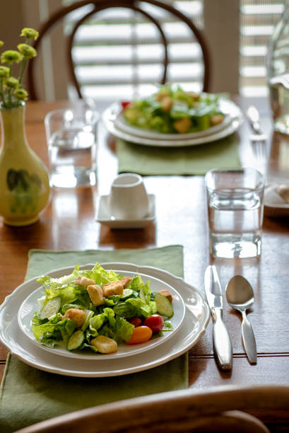 Casual wooden dining room table is set for dinner with plates of salad and water glasses.