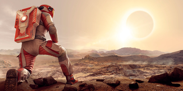 An astronaut kneeling on one leg and resting arm on thigh,  dressed in white and orange spacesuit and backpack on planet Mars. The spaceman is looking out over an empty barren rocky terrain on Mars, at a solar eclipse at sunset in contemplation.