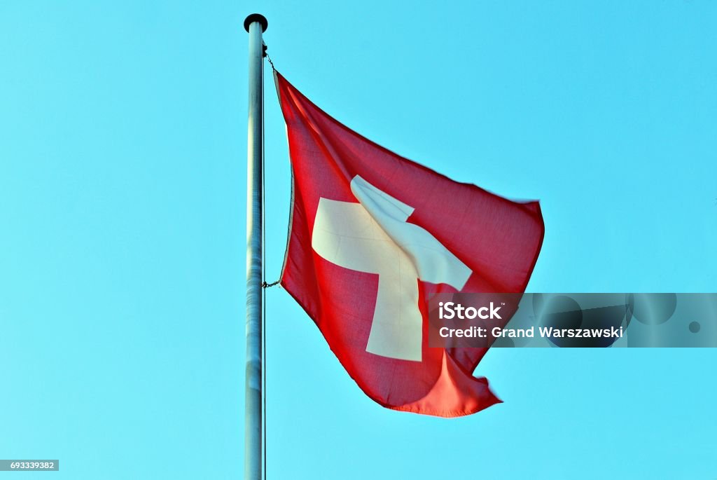 Swiss flag blowing in the wind Red Switzerland national flag on pole waving against clear blue sky Flag Stock Photo