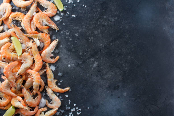 istock Shrimps with lime, ice and sea salt on a black background. Frame for your text. Shrimp with lime and spices scattered on black background. 693349230