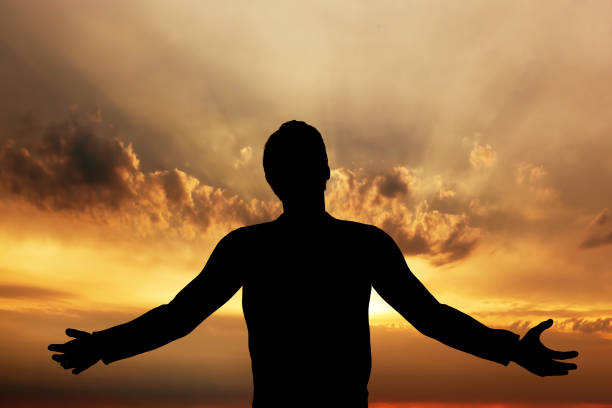 człowiek modlący się, medytujący w harmonii i pokoju o zachodzie słońca - forgiveness praying men silhouette zdjęcia i obrazy z banku zdjęć