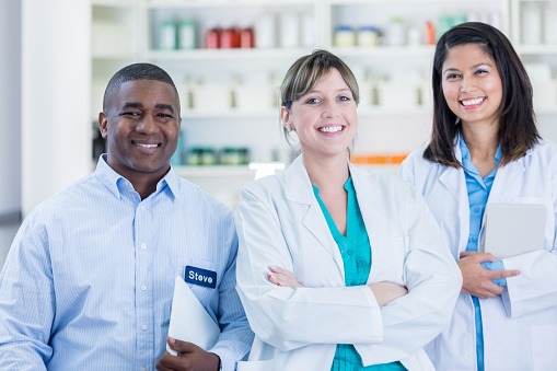 African American pharmacy technician smiles confidently with diverse female pharmacists.