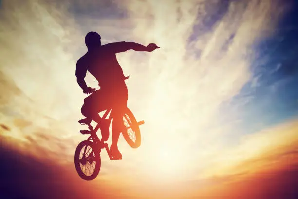 Man jumping on bmx bike performing a trick against sunset sky. Extreme sport