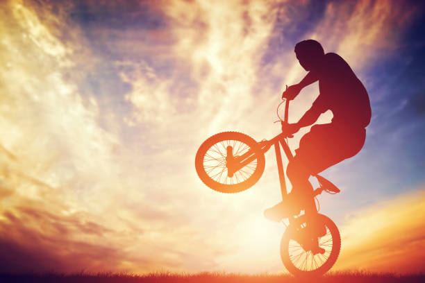 istock Man riding a bmx bike performing a trick against sunset sky 693357166