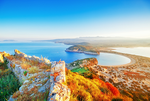 Amazing aerial landscape from Navarino castle ruins above colorful trees and over Voidokilia yellow sand pristine beach by Mediterranean sea, Peloponnese peninsula, Greece. Sunrise scenery, blue sky.
